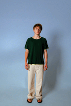 Model wearing the Soleil Lune Base Shirt in forest green with contrast stitching. Made from 55% hemp and 45% organic cotton, featuring a relaxed fit, lightweight natural texture, and soft drape styled with cream trousers in a minimal studio setting.