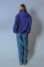 Back view of the Soleil Lune Henley Hoodie in royal blue, showcasing the oversized hood, relaxed silhouette, ribbed hem, and clean minimalist design paired with light wash denim jeans.
