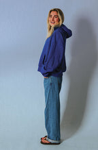 Side profile of the Soleil Lune Henley Hoodie in royal blue, highlighting the oversized fit, spacious hood, drop shoulders, and kangaroo pocket with the model wearing relaxed light wash jeans.
