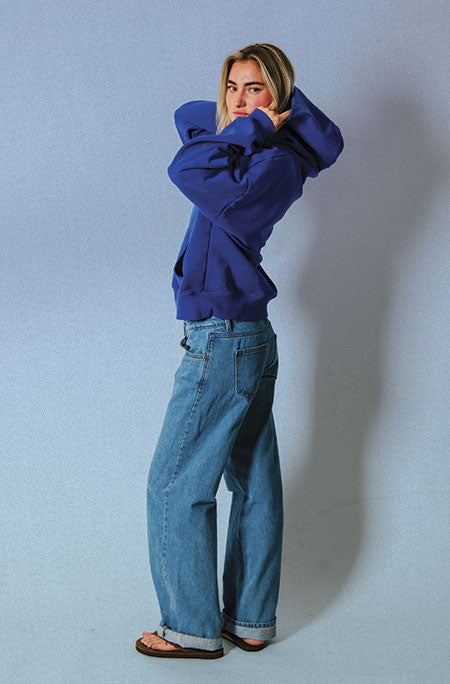 Three-quarter side view of the Soleil Lune Henley Hoodie in royal blue, showing the oversized hood, relaxed fit, and ribbed cuffs as the model poses with the hood resting behind her.